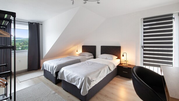 A bedroom with two beds, a desk, a chair, a radiator, and a window with blinds. - Apartment 'Zur Nordhelle' with Mountain View and Wi-Fi (Herscheid)