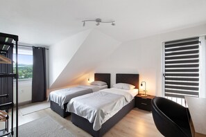 Une chambre avec deux lits, un bureau, une chaise, un radiateur et une fenêtre avec des stores.