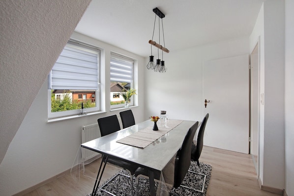 Spiseplads med et bord, stole, en hængende lampe og udsigt gennem vinduet.