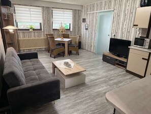 Ett möblerat vardagsrum med en soffa, ett soffbord, ett matbord med stolar, en tv och en mikrovågsugn.