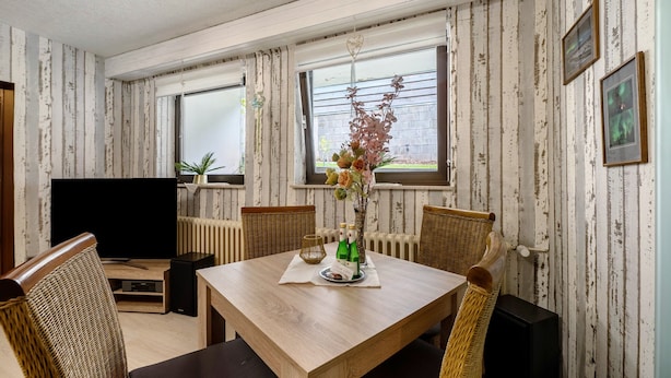 A room with a wooden dining table, wicker chairs, a flat-screen TV, and a window with curtains. - "Pesch" Holiday Apartment with Shared Terrace (Nettersheim -Pesch)