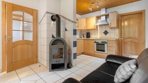 Una cocina con estufa de leña, un comedor con mesa y sillas, y una sala de estar con sofá.
