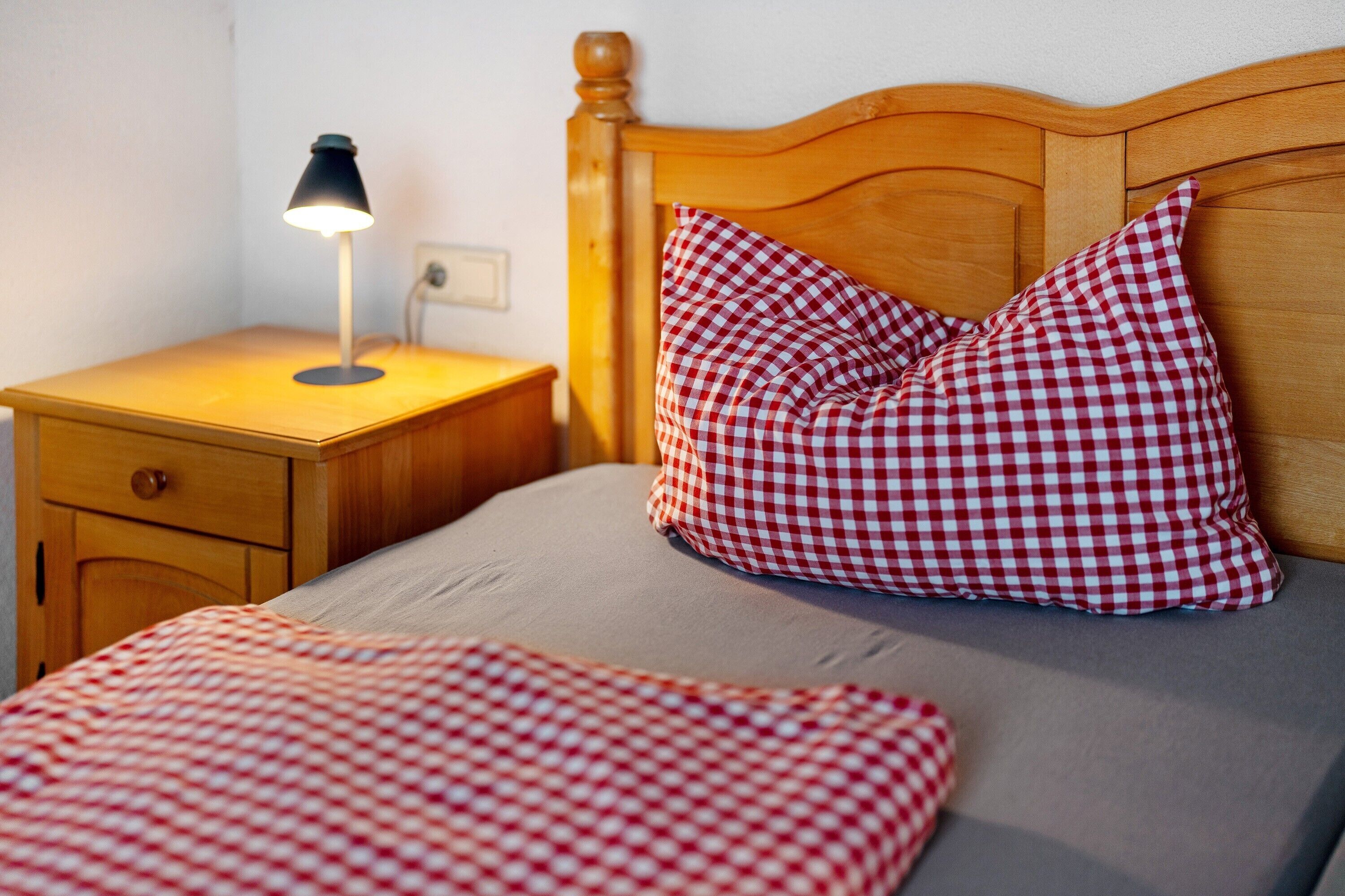 A bed with a checkered pillow, a bedside lamp, and a wooden nightstand.