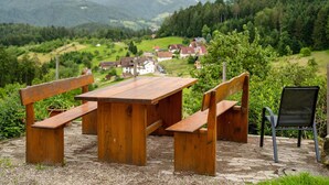 Mesa y bancos de madera al aire libre con vistas a un pueblo y montañas al fondo.
