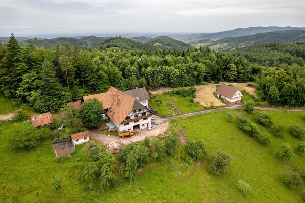 A rural house with a red roof, surrounded by lush greenery and hills in the background.