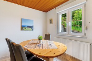 A dining area with a round wooden table, chairs, a small potted plant, and a painting on the wall.