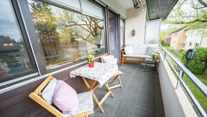 En balkon med et bord og stole, store vinduer og udsigt over det omkringliggende område.