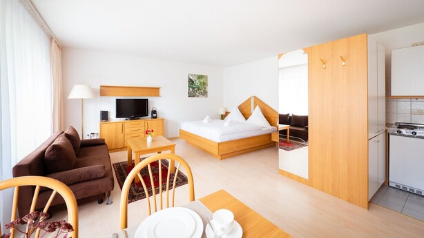 Een hotelkamer met een bed, een televisie, een sofa, een eettafel en een keukenhoek.