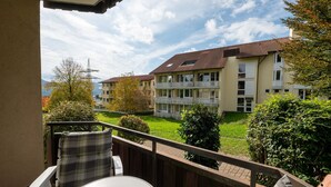 Een balkon met een tafel en stoelen, met uitzicht op een verzorgd gazon en gebouwen met balkons.