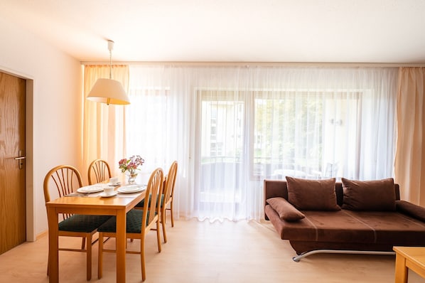 A room with a dining table, chairs, a sofa, and a lamp.