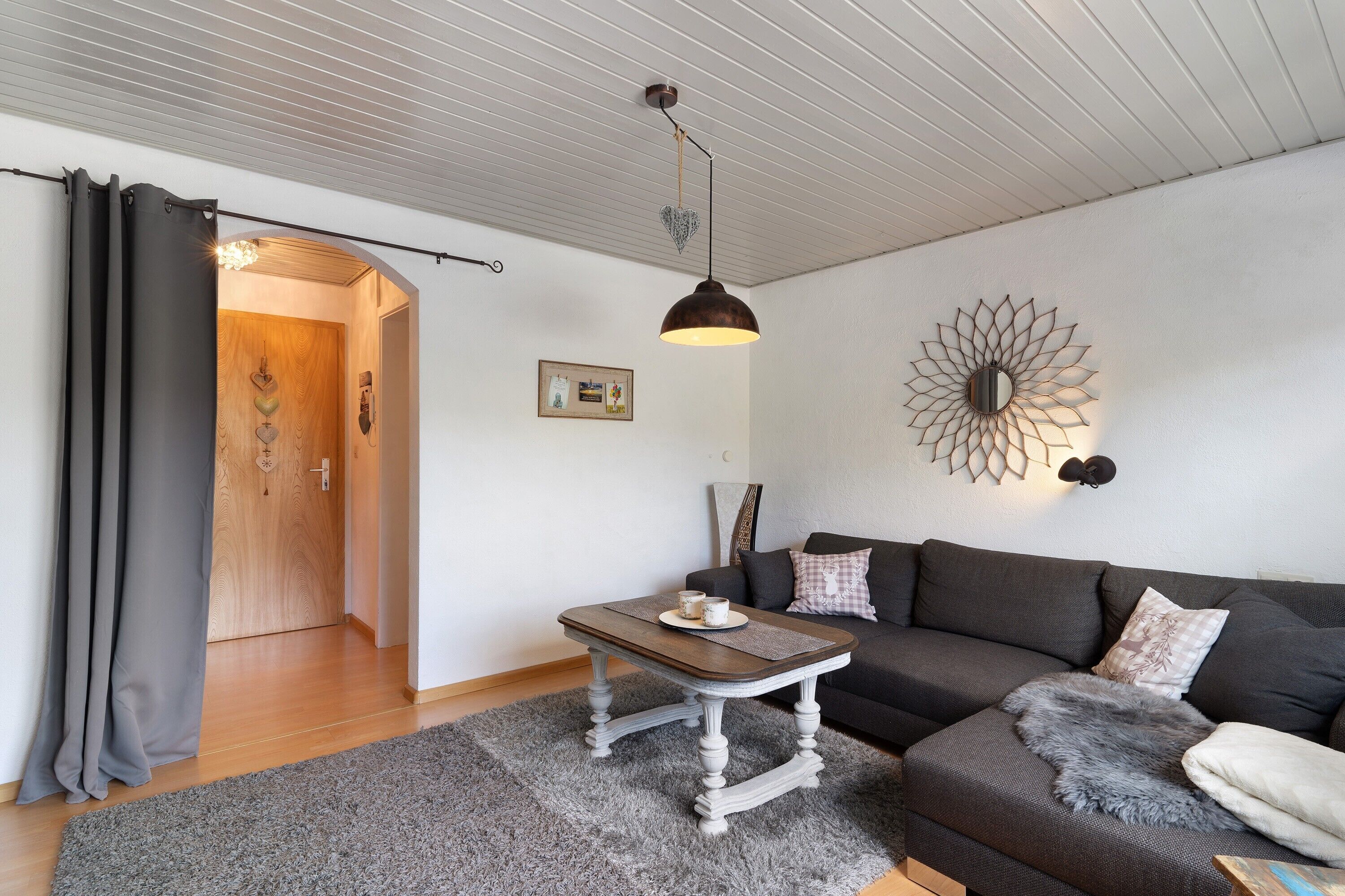 Una sala de estar con un sofá, una mesa de centro, un adorno en la pared y una puerta que da a otra habitación.