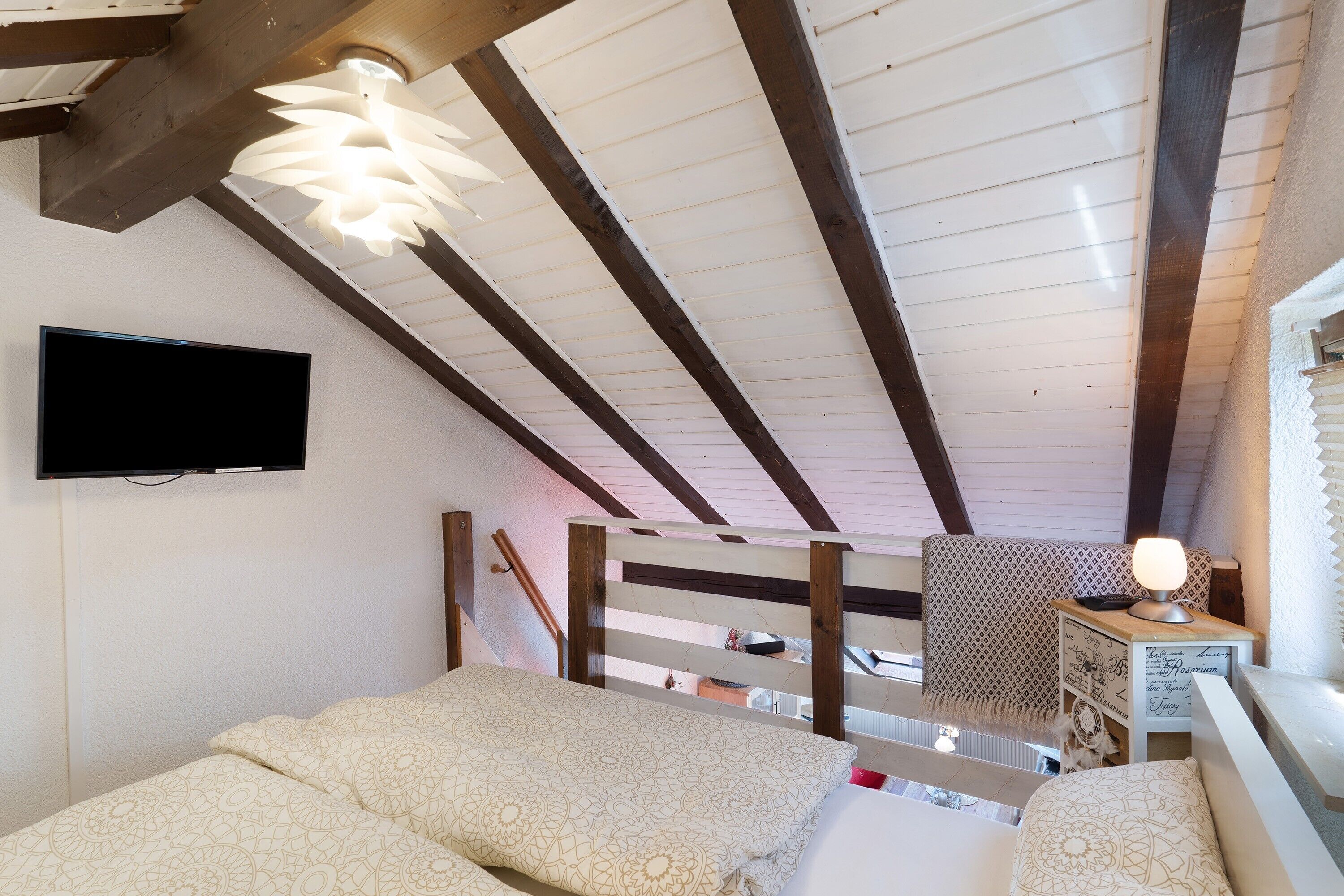 Een slaapkamer met een bed, een tv aan de muur, een plafondventilator en houten balken.