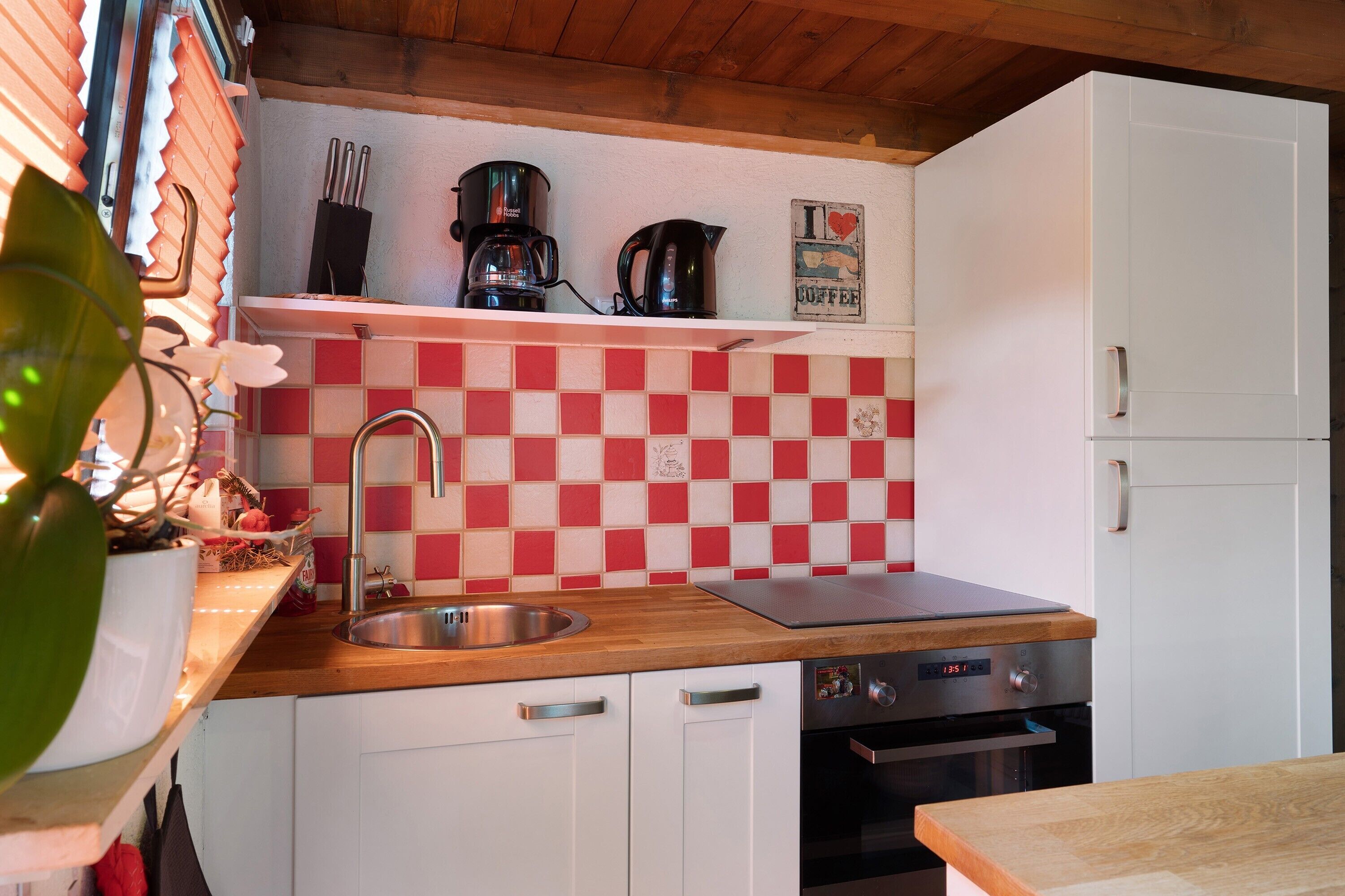 A kitchen with a checkered backsplash, a coffee maker, a kettle, and a refrigerator.