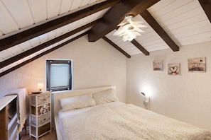 A bedroom with a sloped ceiling, a bed with patterned bedding, a bedside lamp, a window with blinds, and wall decorations.