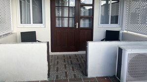 A house entrance with a brown door, two windows with white frames, and a white air conditioning unit to the right. - St. Lawrence Suites - Suite Three (Oistins)