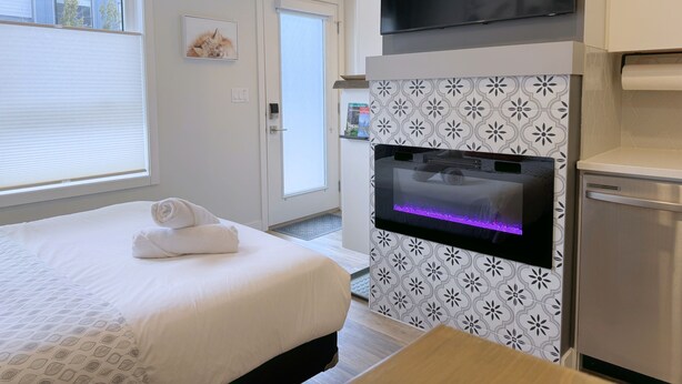 A hotel room with a bed, a flat-screen TV, a built-in oven, and a window with blinds. - 🦊Tiny, Mighty Studio in Canmore🦊  (Canmore)