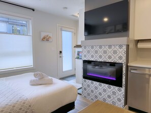 A hotel room with a bed, a flat-screen TV, a built-in oven, and a window with blinds. - 🦊Tiny, Mighty Studio in Canmore🦊  (Canmore)