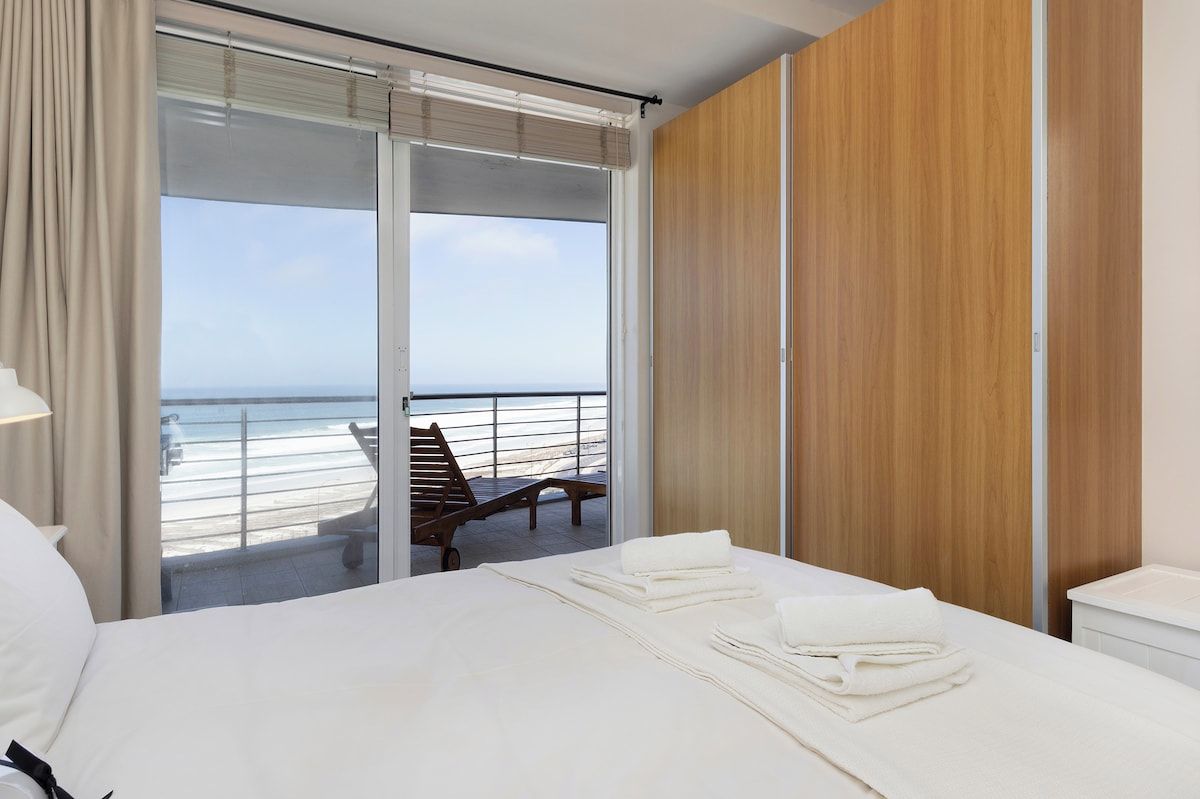 Ein Hotelzimmer mit Bett, einem Holzschrank, einem Balkon mit Meerblick und einem Sessel.