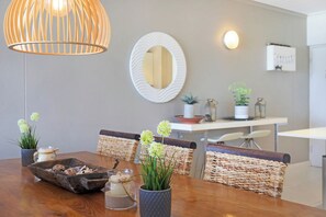 A dining area with a wooden table, wicker chairs, a decorative mirror, and a hanging light fixture.