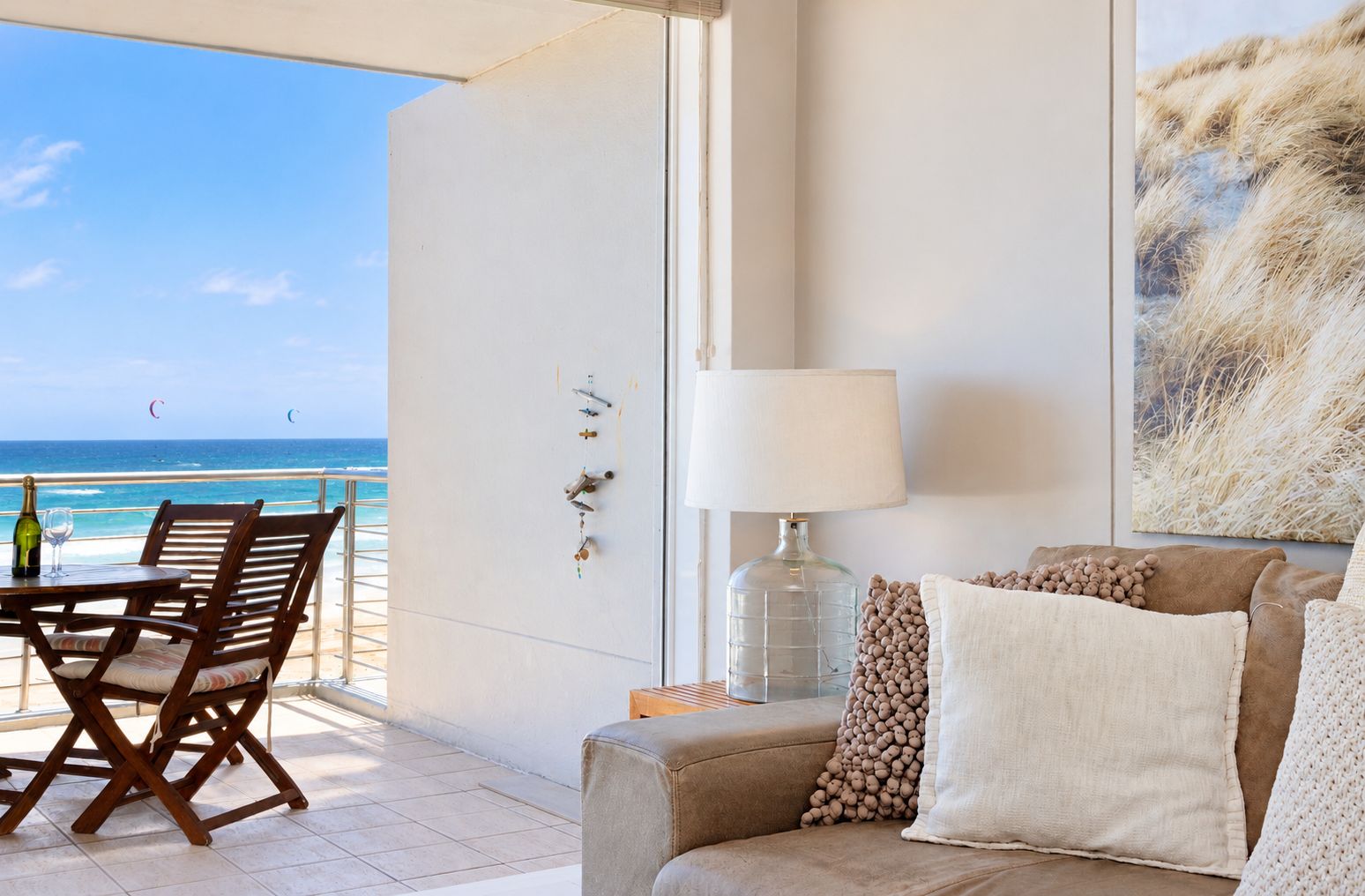 A balcony with a view of the ocean, a table with chairs, a sofa with cushions, a lamp, and a wall-mounted light fixture.