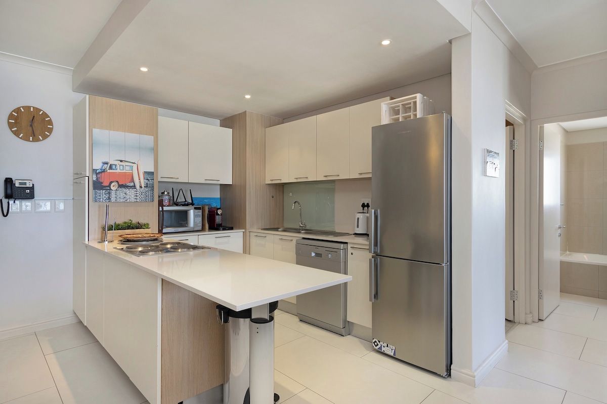 Een moderne keuken met een centraal eiland, roestvrijstalen apparatuur en een klok aan de muur.