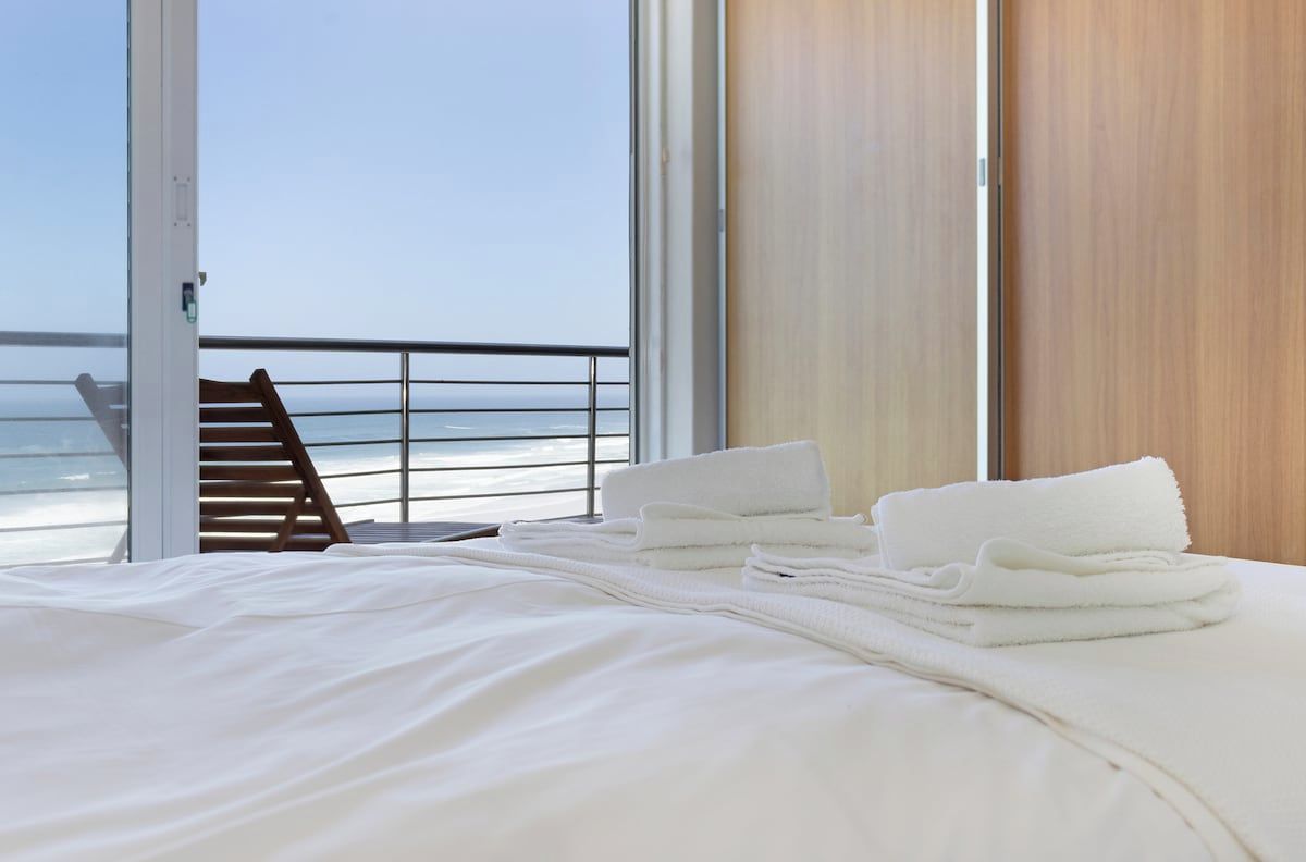 Ein Hotelzimmer mit einem Bett, einem Holzstuhl und Blick auf den Ozean.
