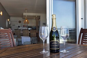 A bottle of sparkling wine and two glasses on a wooden table with a view of a balcony. - Beachfront Apt - Kite Beach + table mtn view (Cape Town)