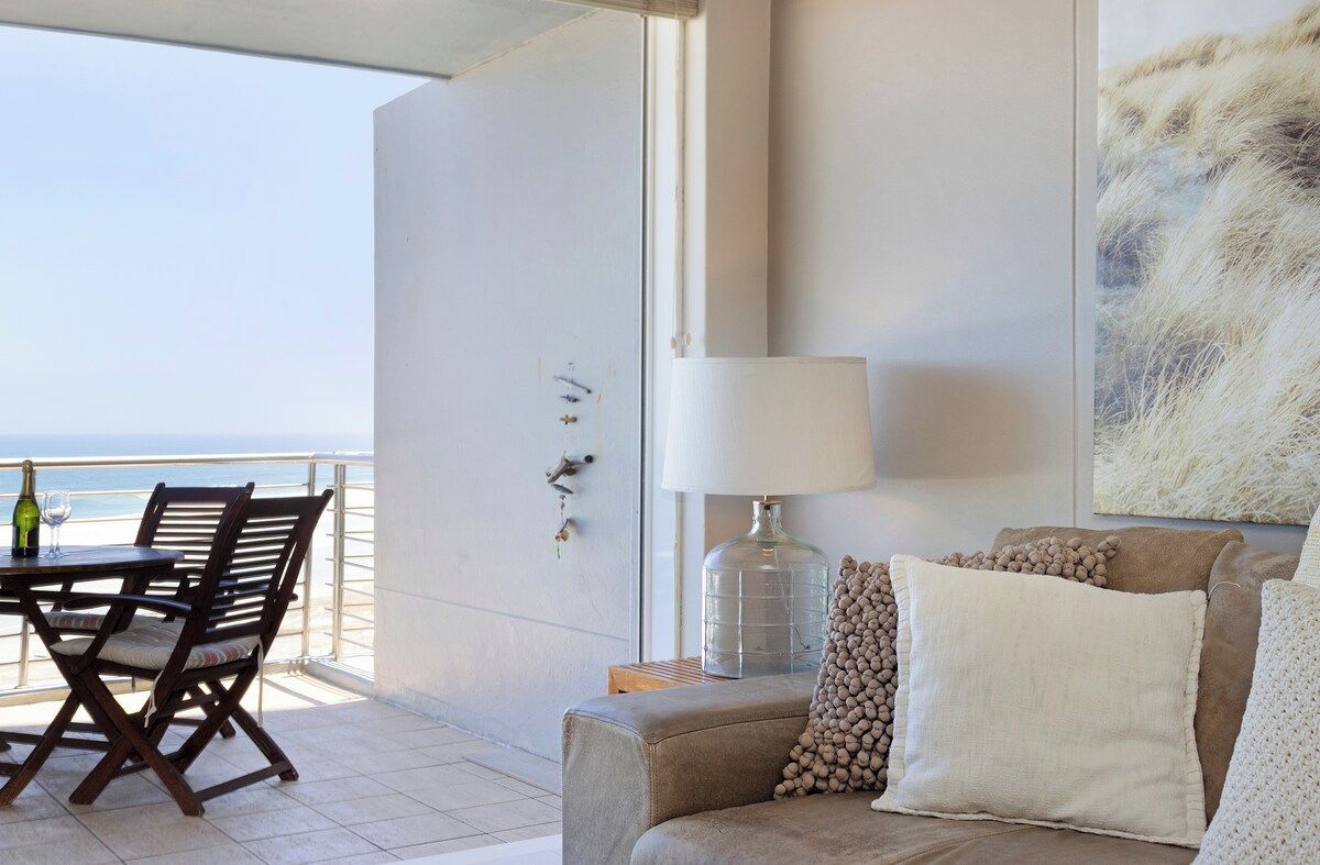 A balcony with a table and chairs, a sofa, a lamp, and a painting.