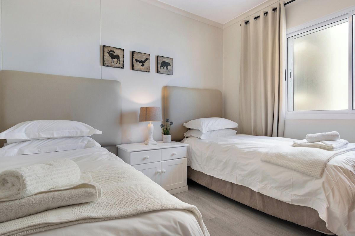 Une chambre d’hôtel avec deux lits, une table de chevet avec une lampe et une fenêtre avec des rideaux.