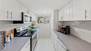 Cocina moderna con armarios blancos, electrodomésticos de acero inoxidable y una ventana que ofrece vistas de edificios cercanos.