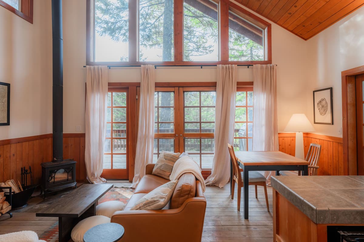 A cozy cabin interior with a wooden table, sofa, and a fireplace.