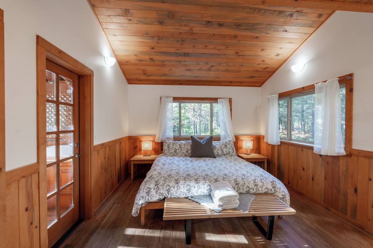 A wooden-paneled bedroom with a bed, bedside lamps, and a window with curtains.