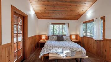 A wooden-paneled bedroom with a bed, bedside lamps, and a window with curtains.