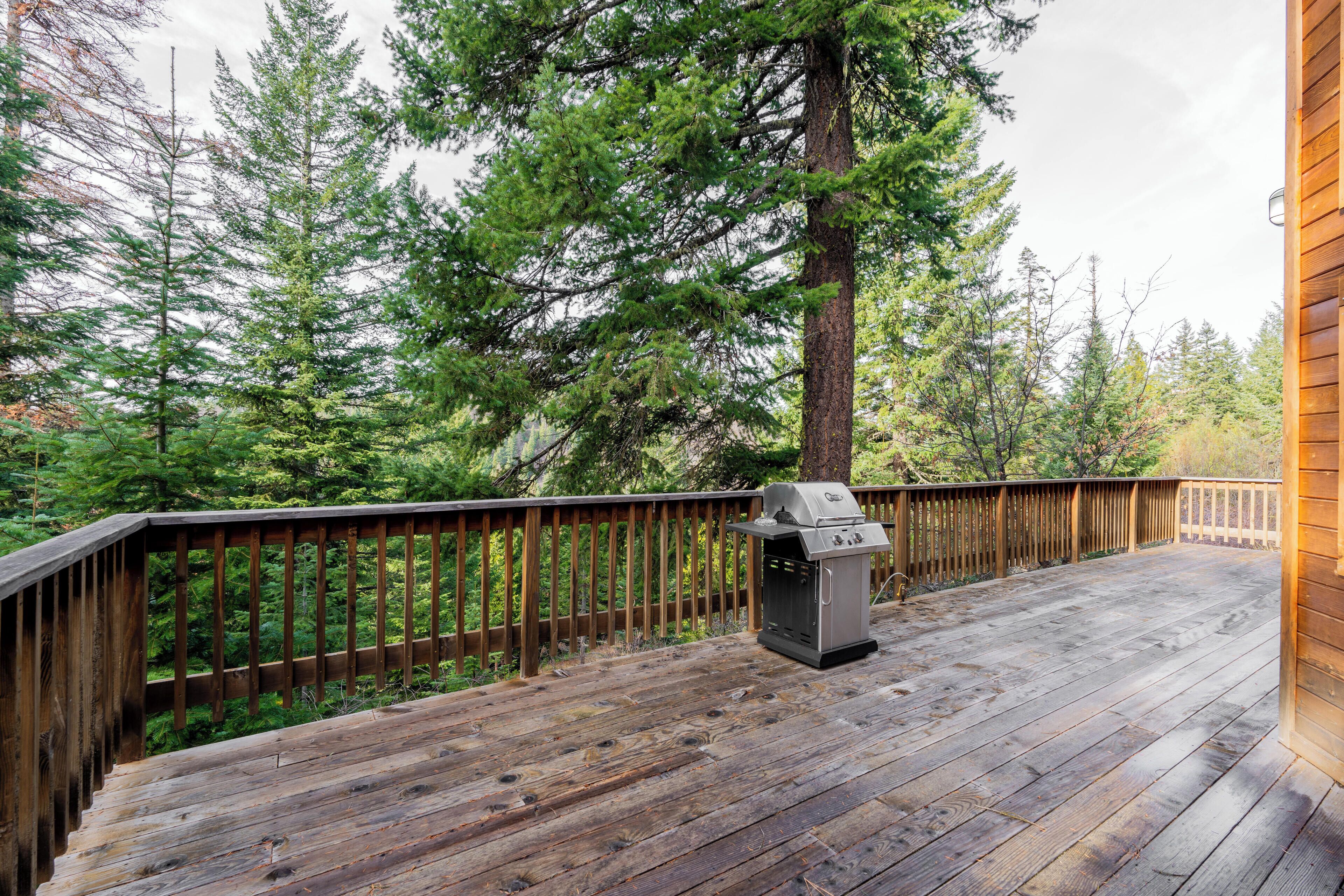 A wooden deck with a grill, surrounded by tall trees.