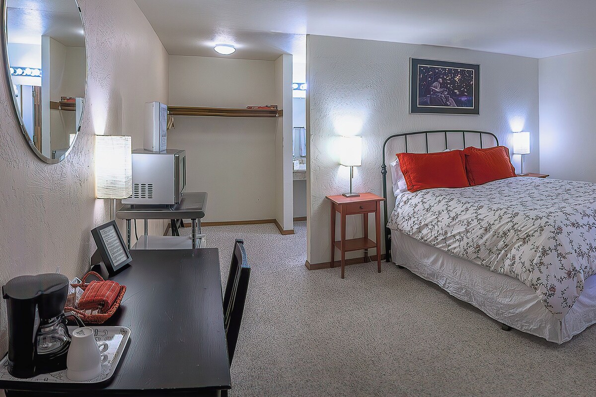 A bedroom with a bed, a desk with a computer, a lamp, and a mirror.