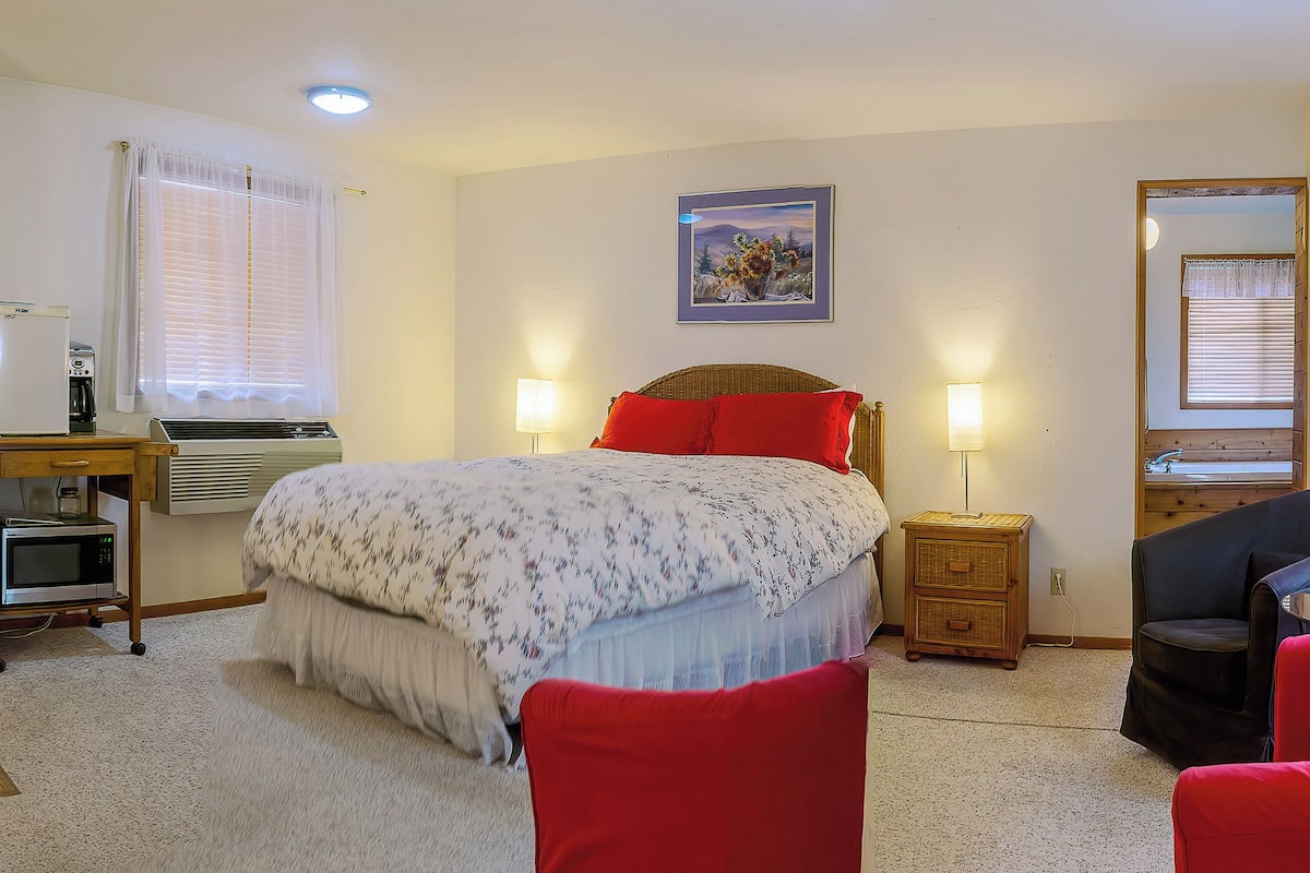 A bedroom with a bed, a desk, a chair, a lamp, and a picture on the wall.