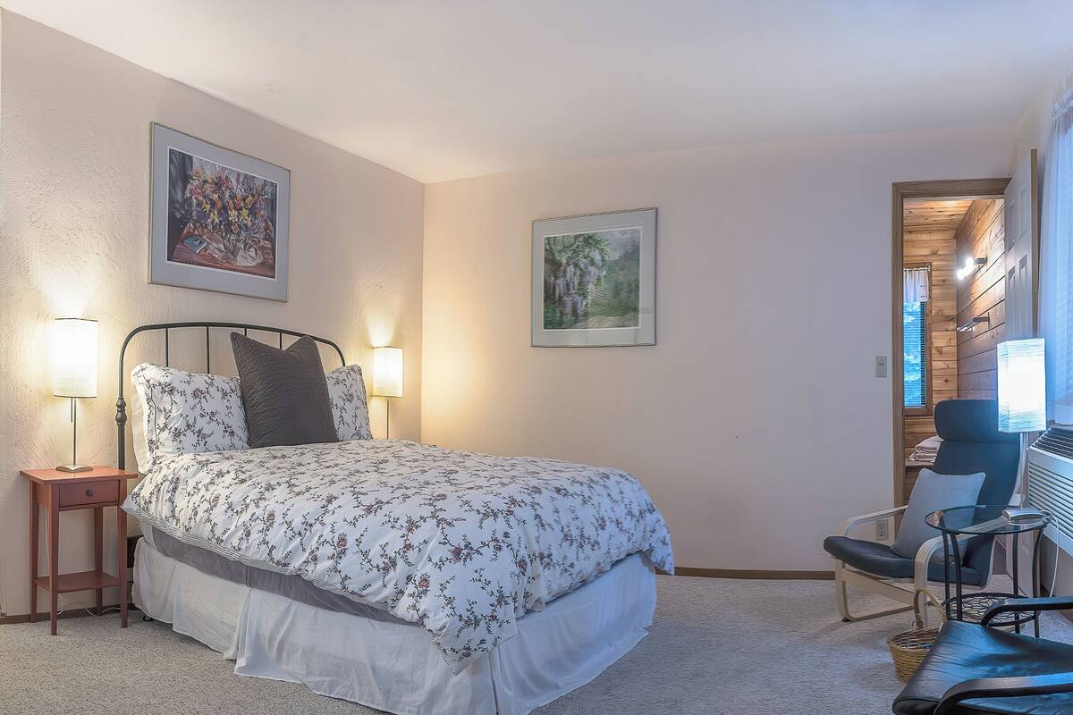 A bedroom with a bed, bedside lamps, a chair, and a desk with a computer.