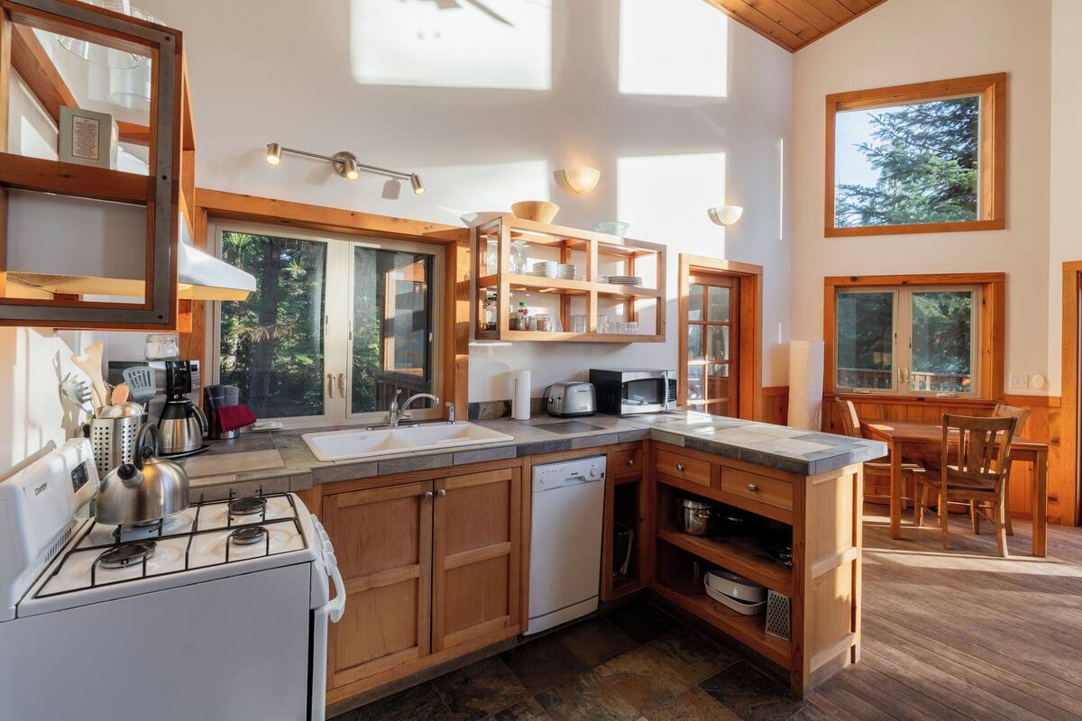 A modern kitchen with wooden cabinets, a gas stove, a dishwasher, and a dining area with a table and chairs.