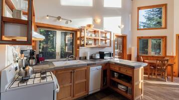 A modern kitchen with wooden cabinets, a gas stove, a dishwasher, and a dining area with a table and chairs.