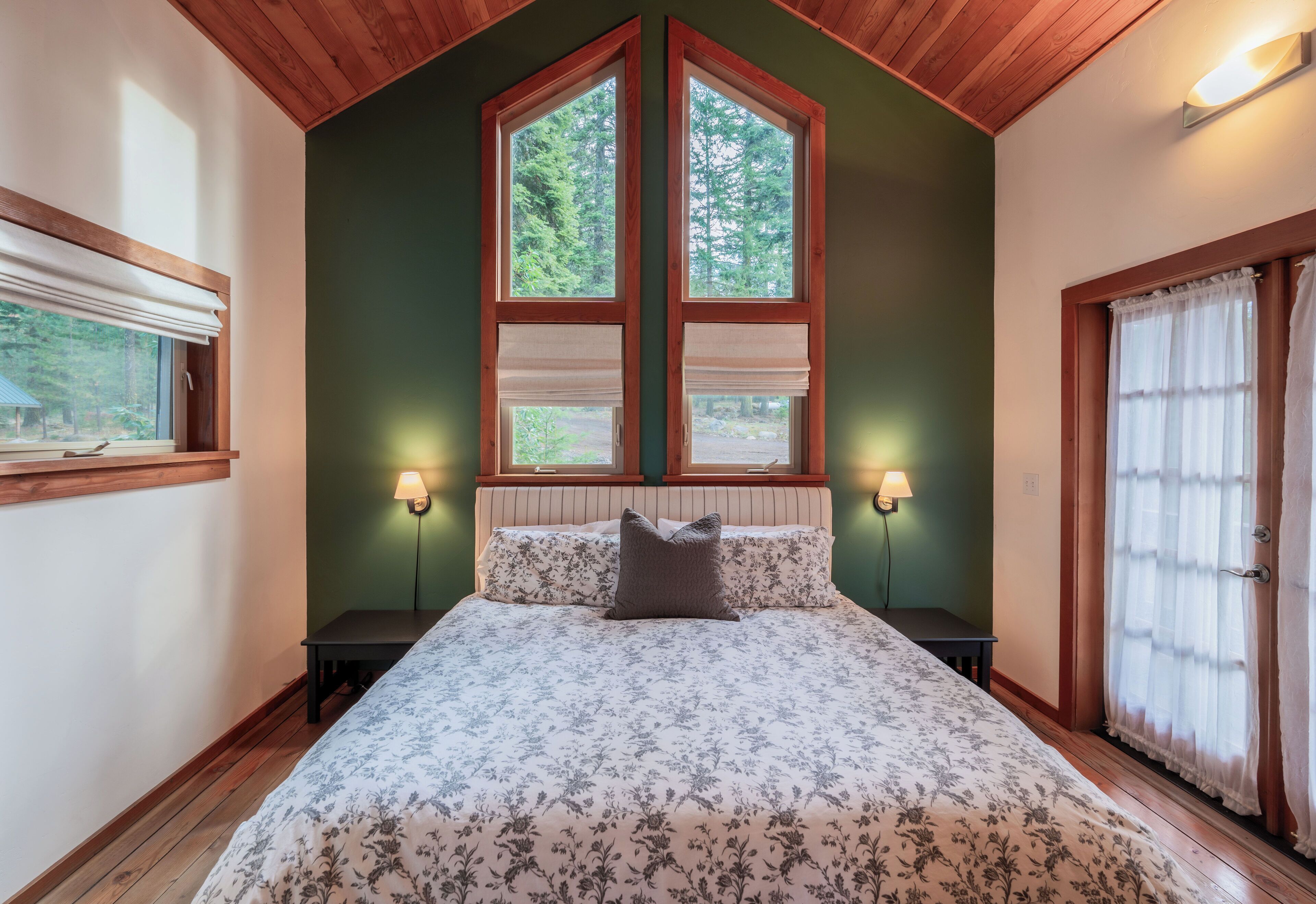 A bedroom with a large bed, two bedside lamps, a window with blinds, and a door with curtains.