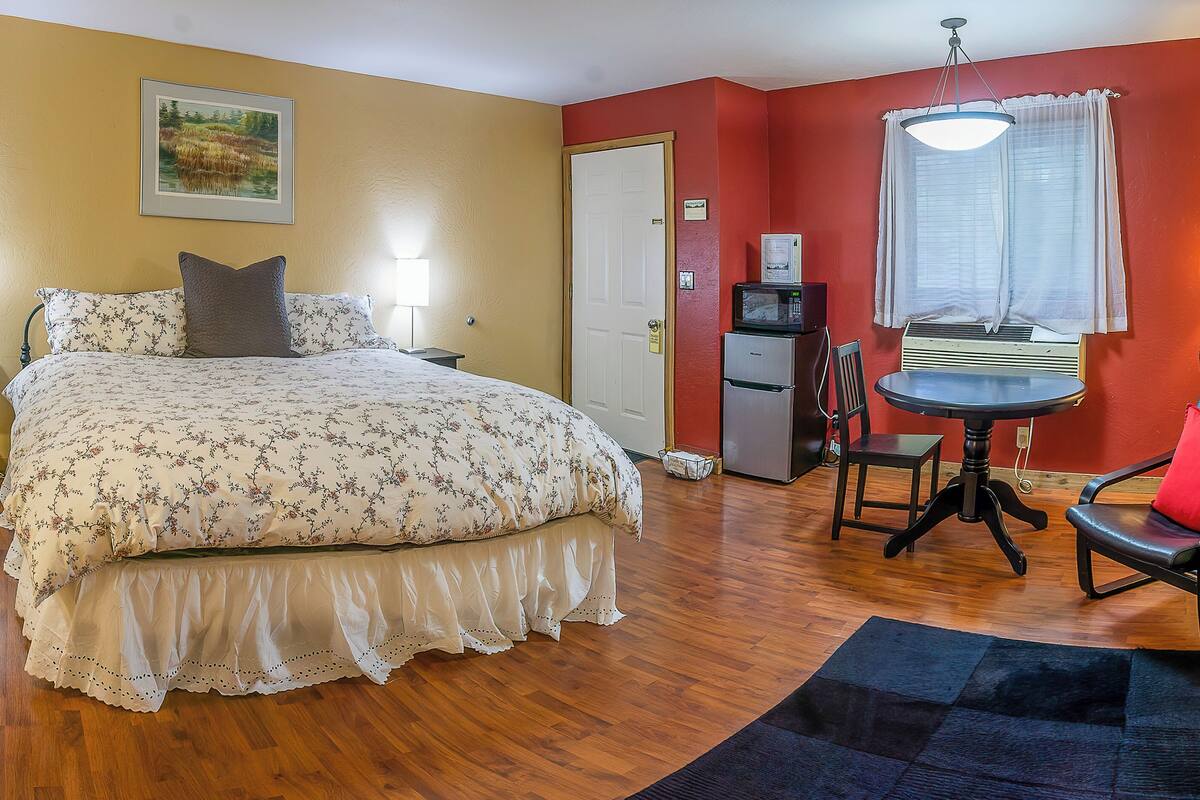 A hotel room with a bed, a desk with a chair, a refrigerator, and a window with curtains.