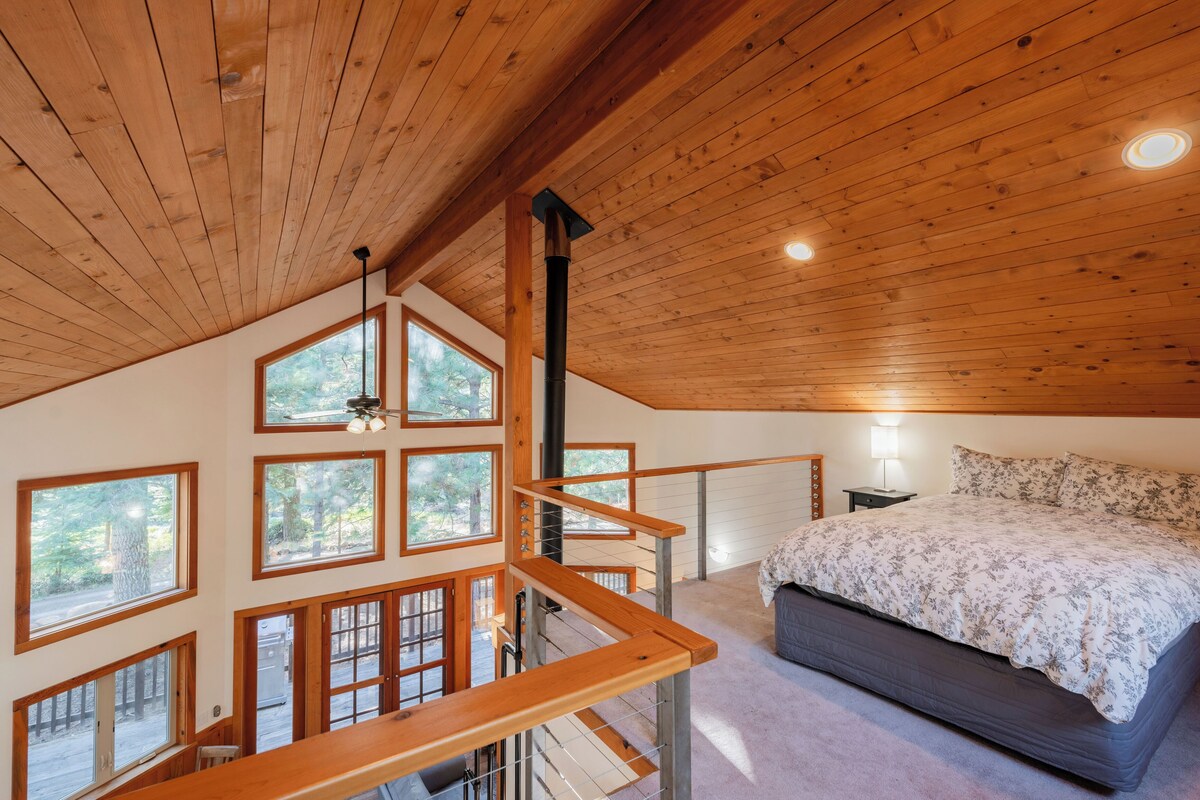 A bedroom with a large bed, wooden ceiling, and multiple windows.