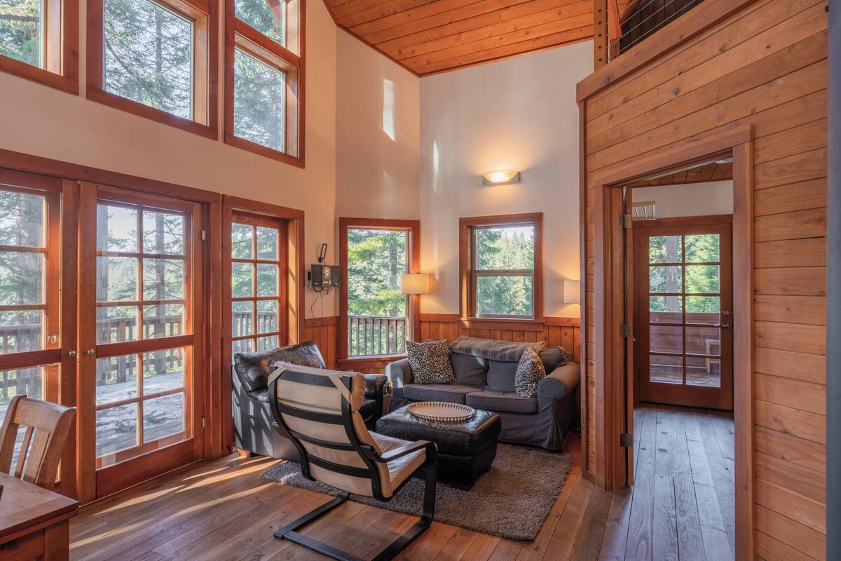 A spacious living area with large windows, a sofa, a chair, and a wooden floor.