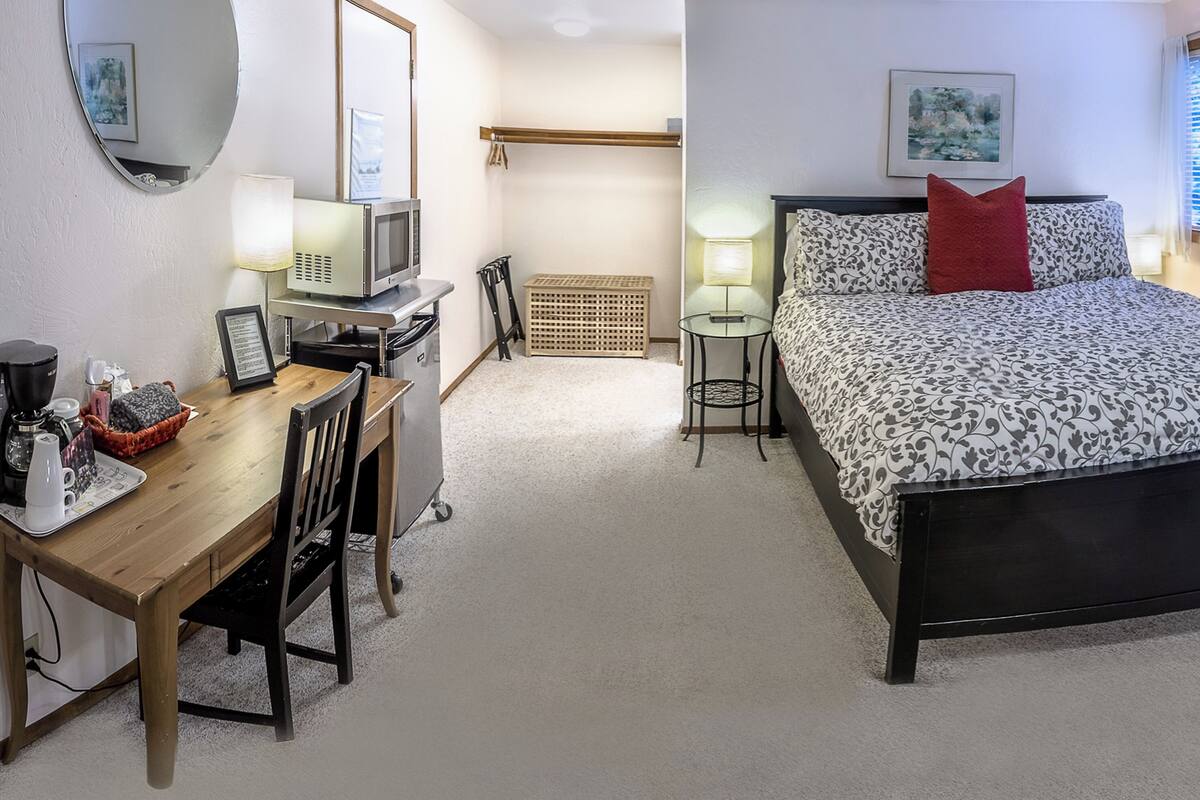 A hotel room with a bed, a desk with a computer, a chair, a small table, and a microwave.