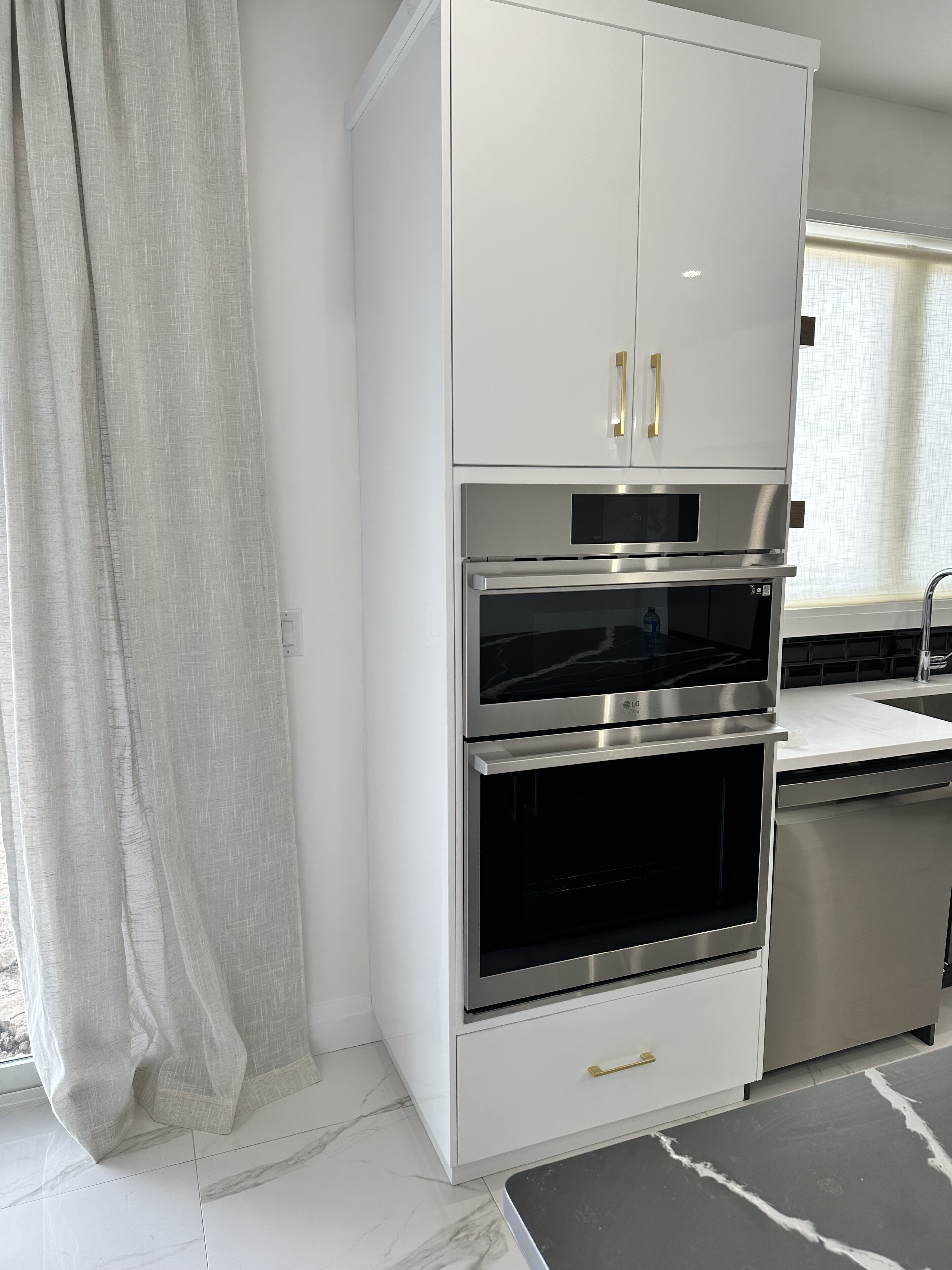 Una cocina moderna con electrodomésticos de acero inoxidable, armarios blancos y piso de mármol.