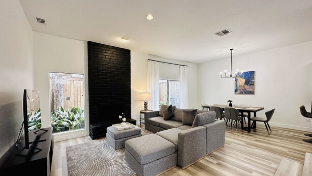 A modern living room with a sectional sofa, a flat-screen TV, a fireplace, and a dining area. - StarryNight @ Museum Park -WORLD CUP- Walk to Museums, Hermann Park, Zoo, Dining (Houston)