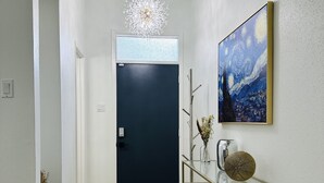 A hallway with a dark door, a chandelier, a painting, and a glass console table. - StarryNight @ Museum Park -WORLD CUP- Walk to Museums, Hermann Park, Zoo, Dining (Houston)