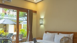 Ein Hotelzimmer mit einem Bett, einem Laptop und einem Strohhut auf den Kissen. Der Balkon bietet Stühle und einen Tisch.