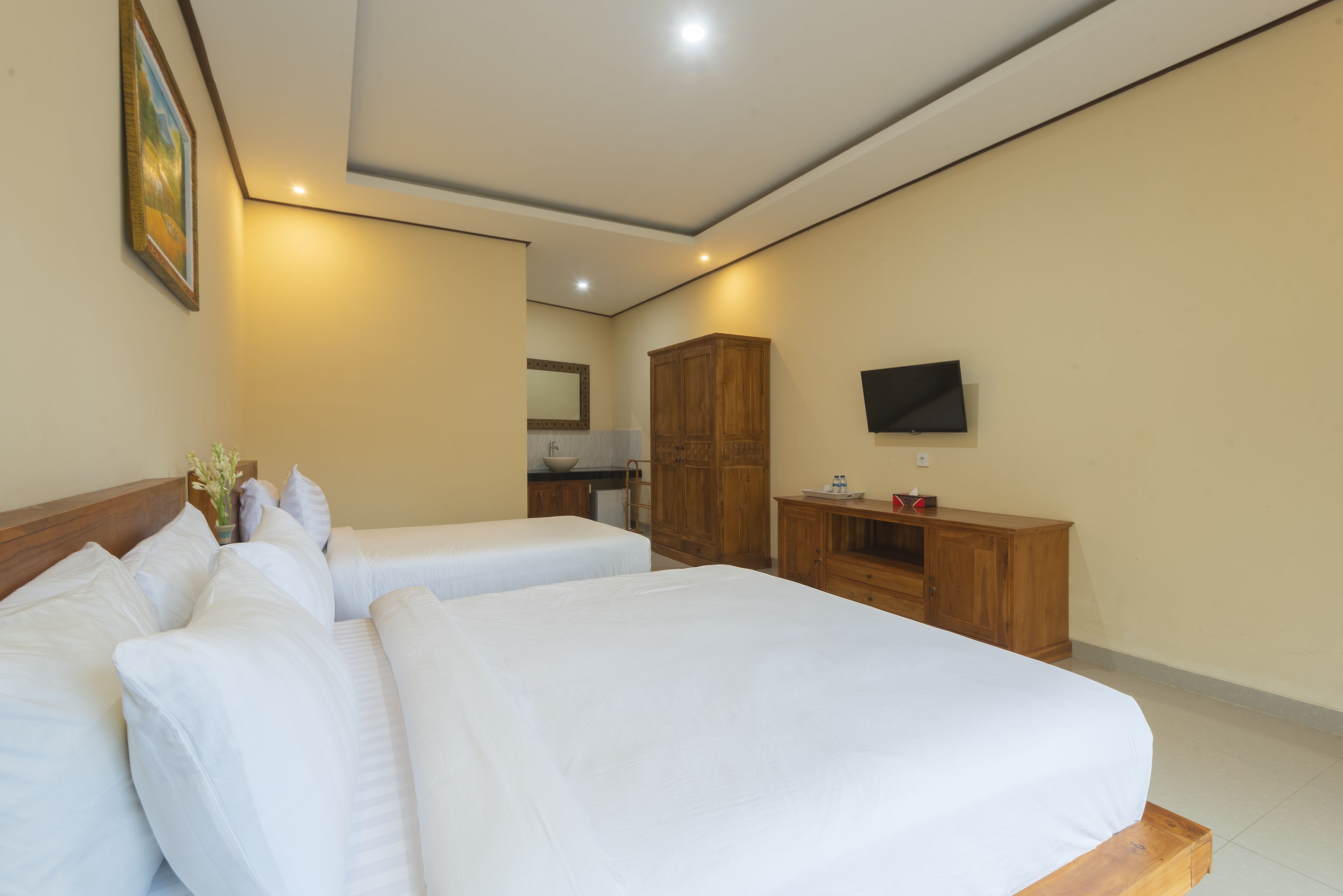 Una habitación de hotel con dos camas, un armario de madera, un televisor y una pequeña kitchenette.