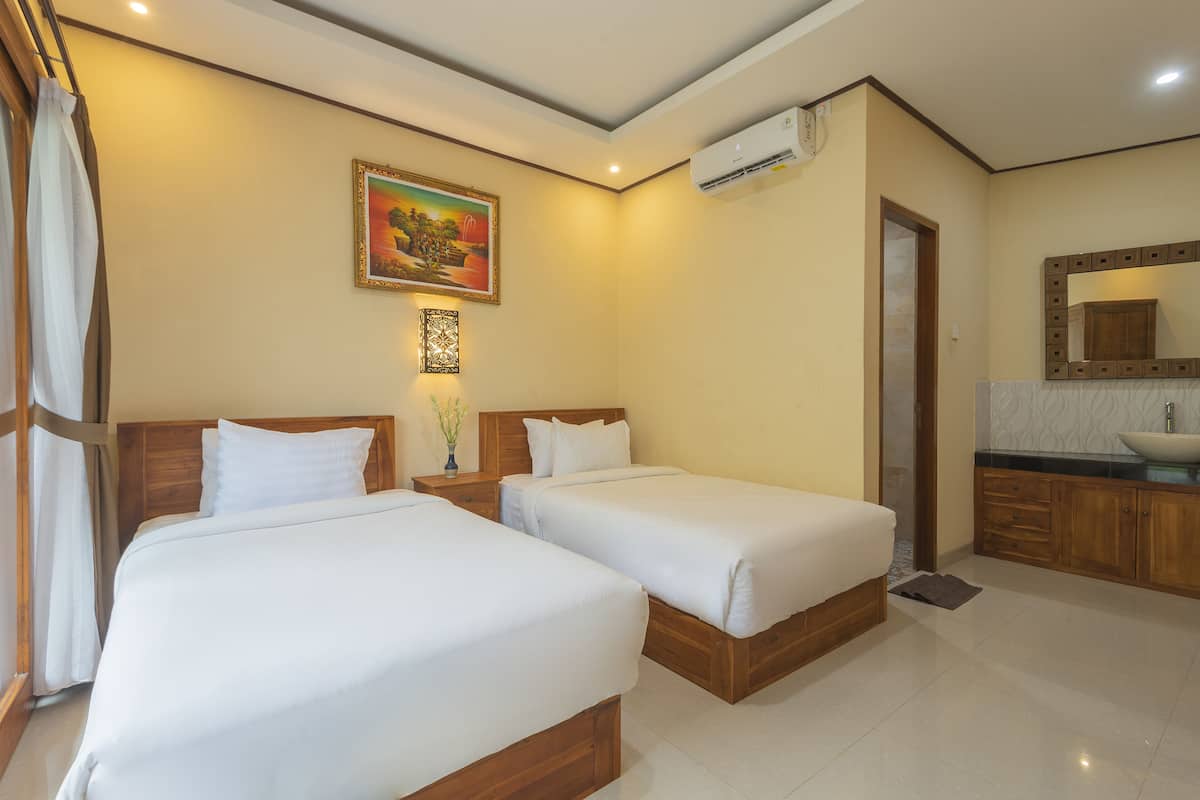 Habitación de hotel con dos camas, un cuadro, aire acondicionado, un espejo y un baño con lavamanos.